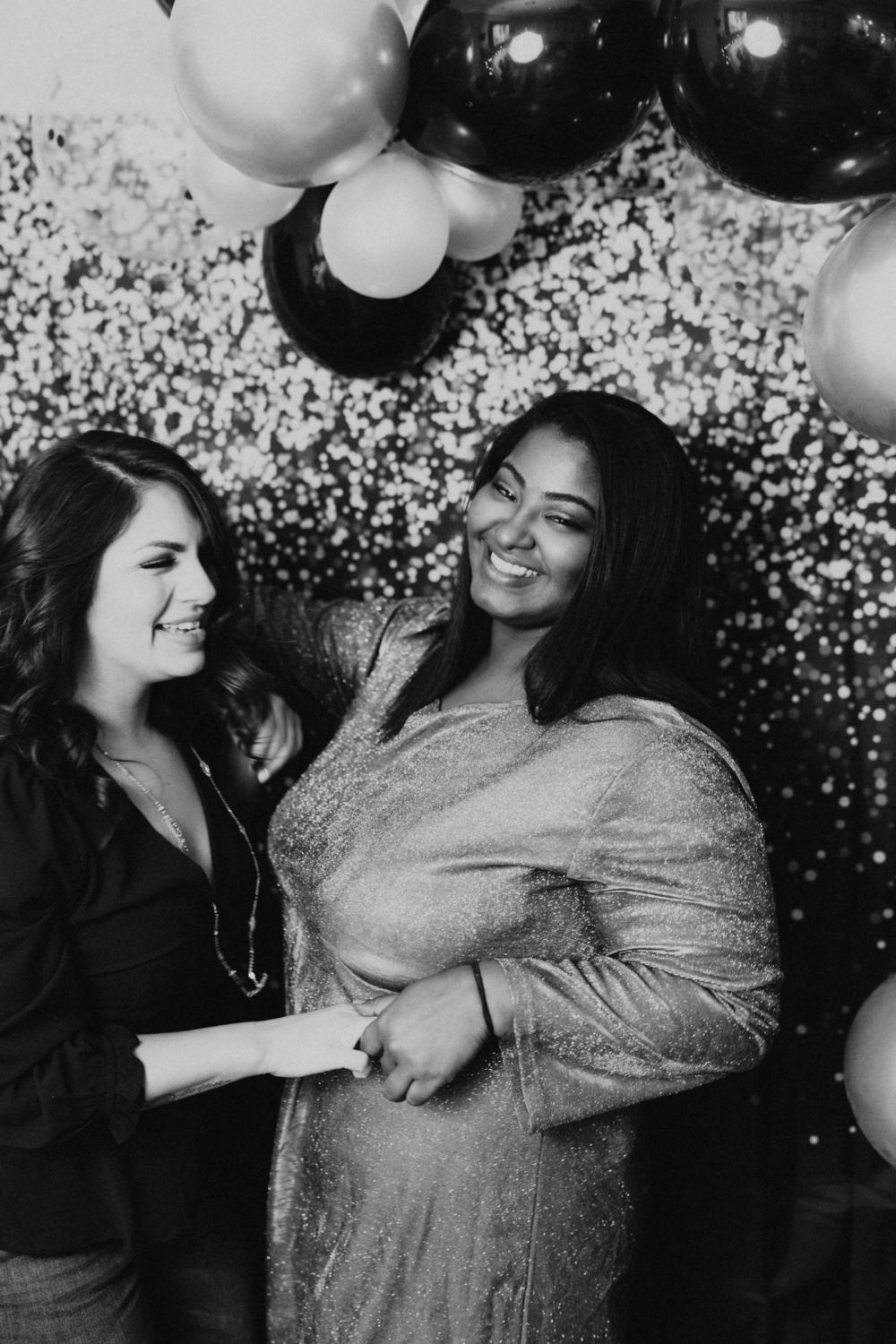 Two friends smiling at a sequin photo booth backdrop